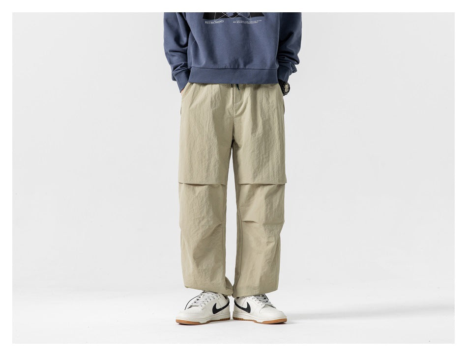 Model wearing loose beige pants with layered knee panels and a wide-leg cut.