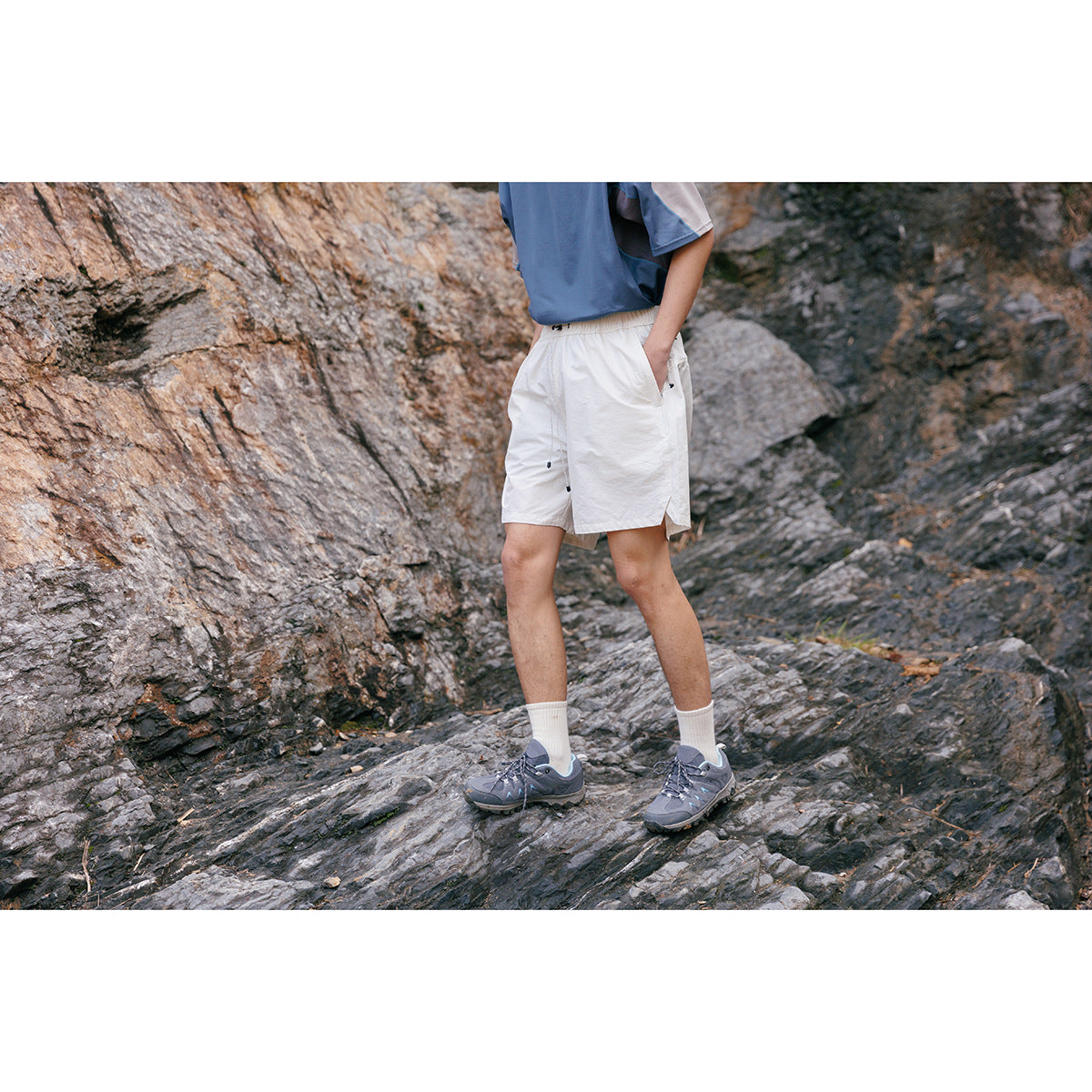 Cropped model standing on rocks in white elastic-waist shorts with a blue top.