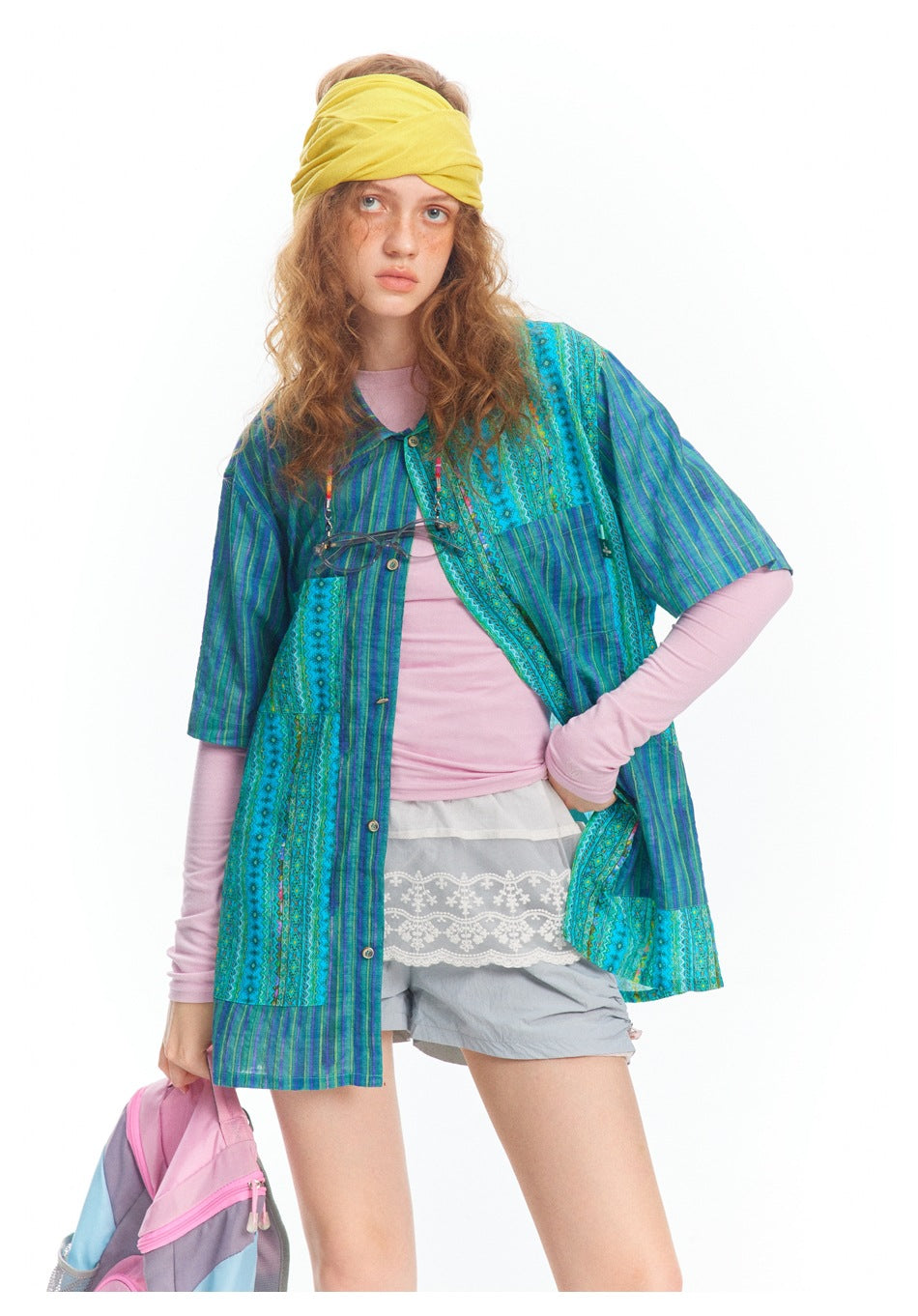 Model wearing an open blue and turquoise patterned tunic over a pink top and gray shorts.