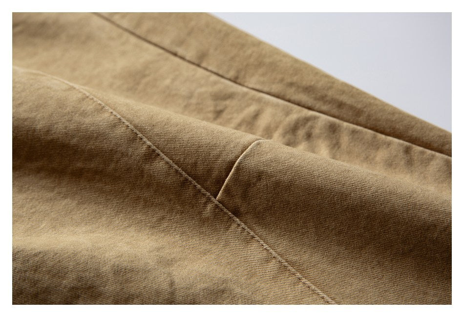 Close-up of tan garment fabric with a diagonal stitched seam and folded edge.