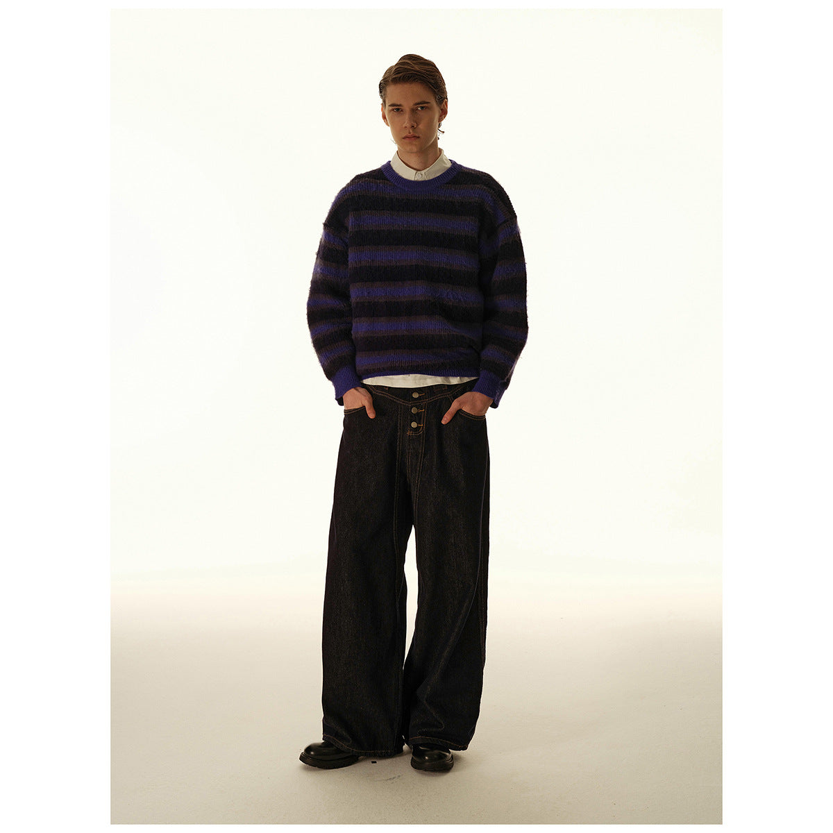 Model wearing a black and purple striped crewneck sweater with dark wide-leg jeans, front view.