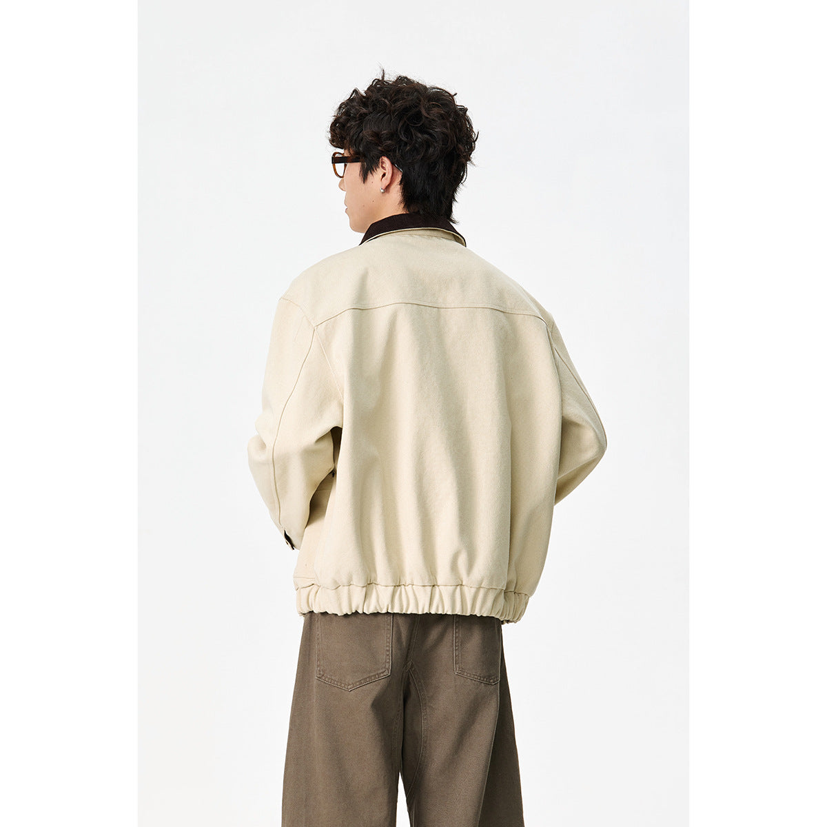 Rear view of a model wearing a cream jacket with a dark collar and gathered hem.