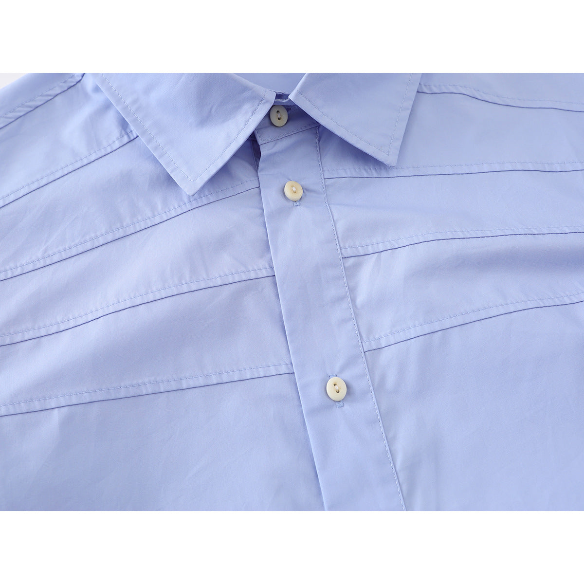Close-up of a light blue shirt's button placket and horizontal stitched front panels.