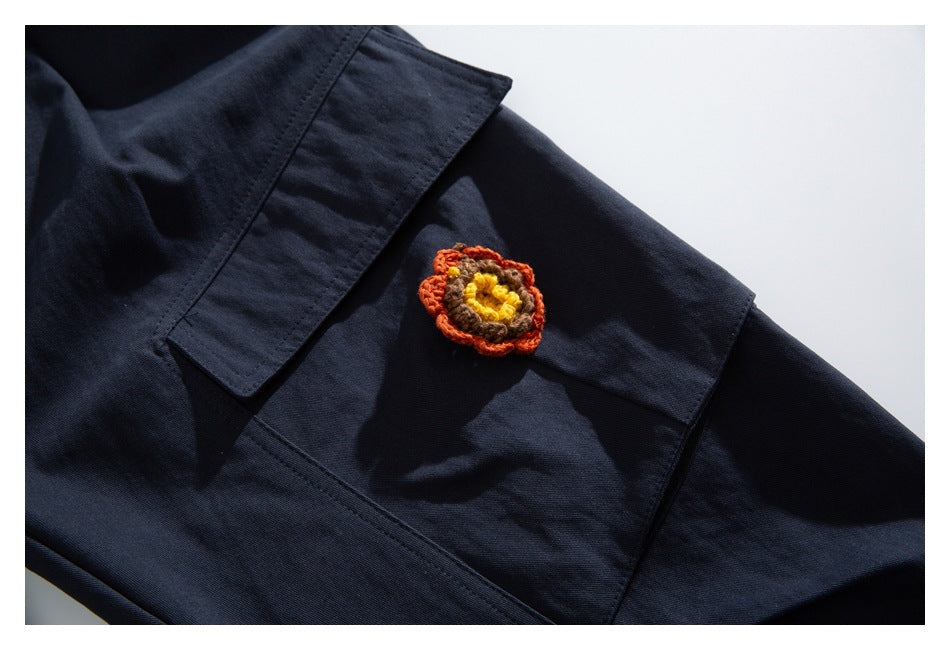 Close-up of a dark navy patch pocket with a small orange, brown and yellow crocheted flower.