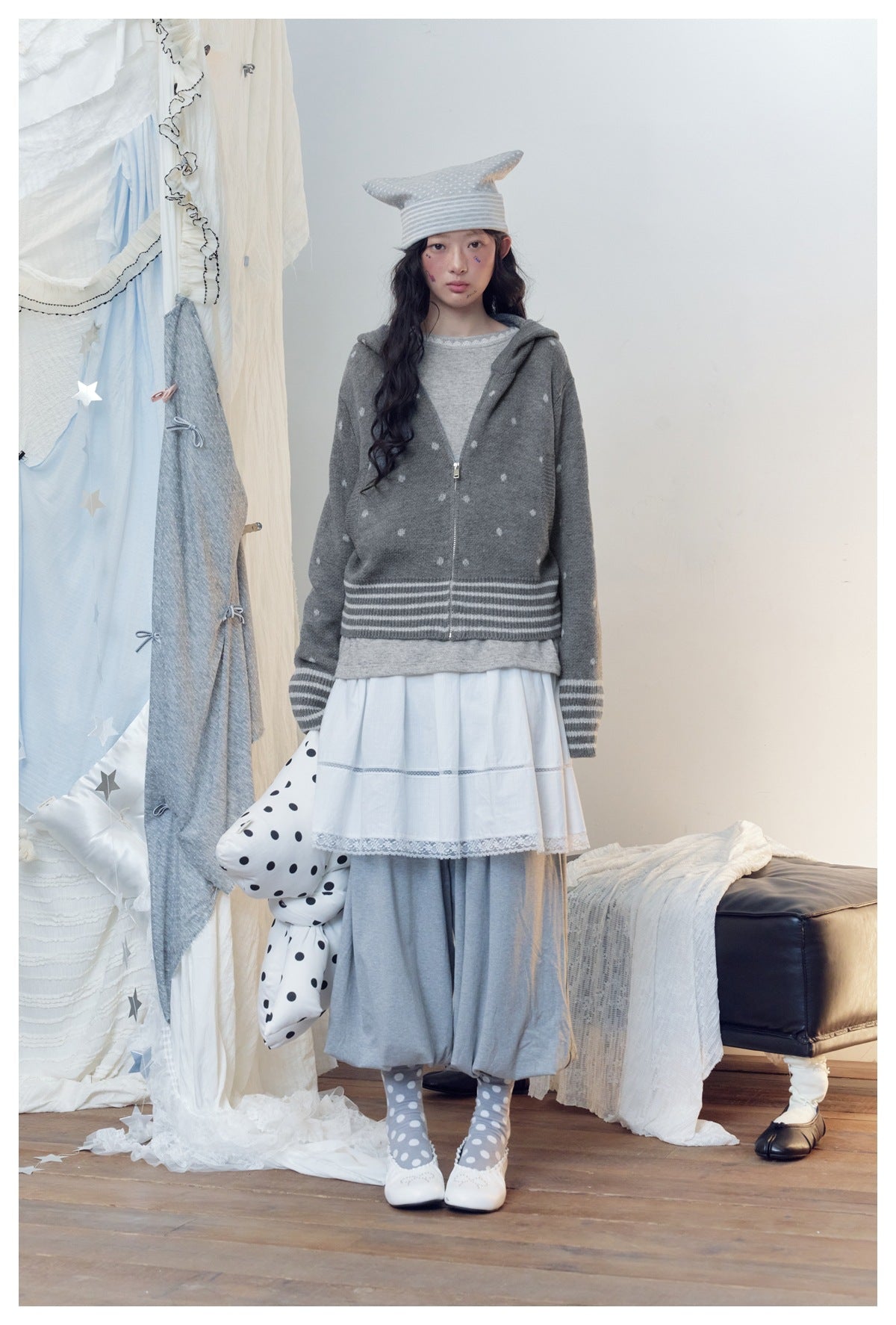 Model wearing gray polka-dot zip hooded knit jacket with striped hem over a gray top, white skirt and gray pants