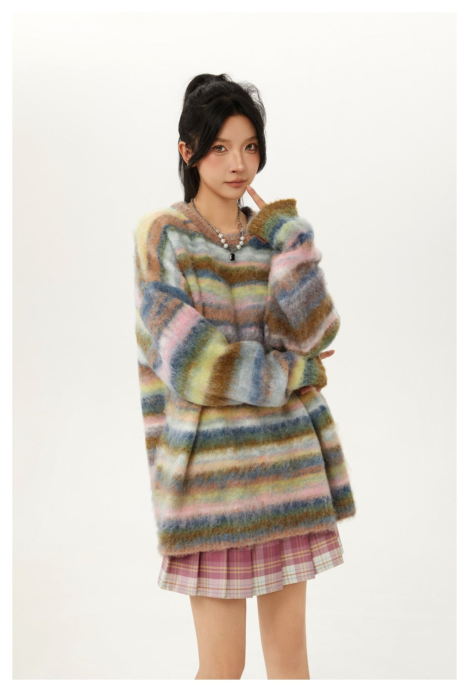 Waist-up view of a model wearing an oversized fuzzy sweater with multicolor horizontal stripes over a pink plaid skirt.