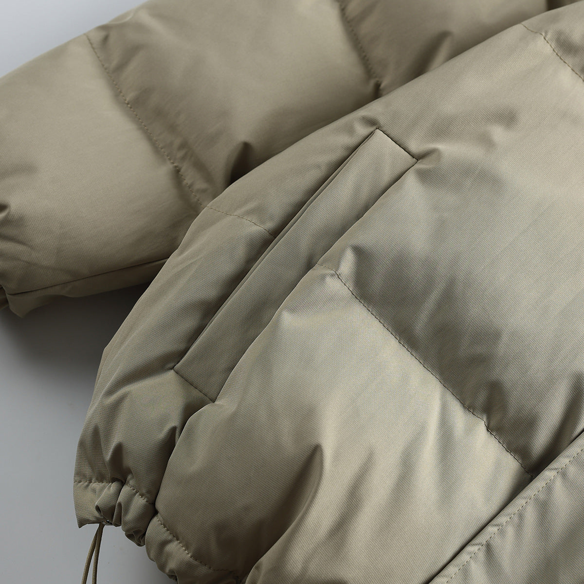 Close-up of a taupe puffer jacket sleeve and seam details, including an elastic cuff and drawcord.
