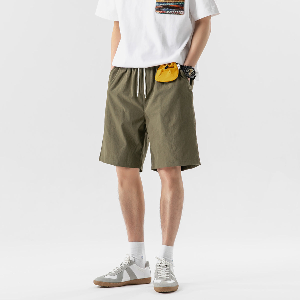 Cropped model wearing olive drawstring shorts with a white T-shirt and sneakers, front view.