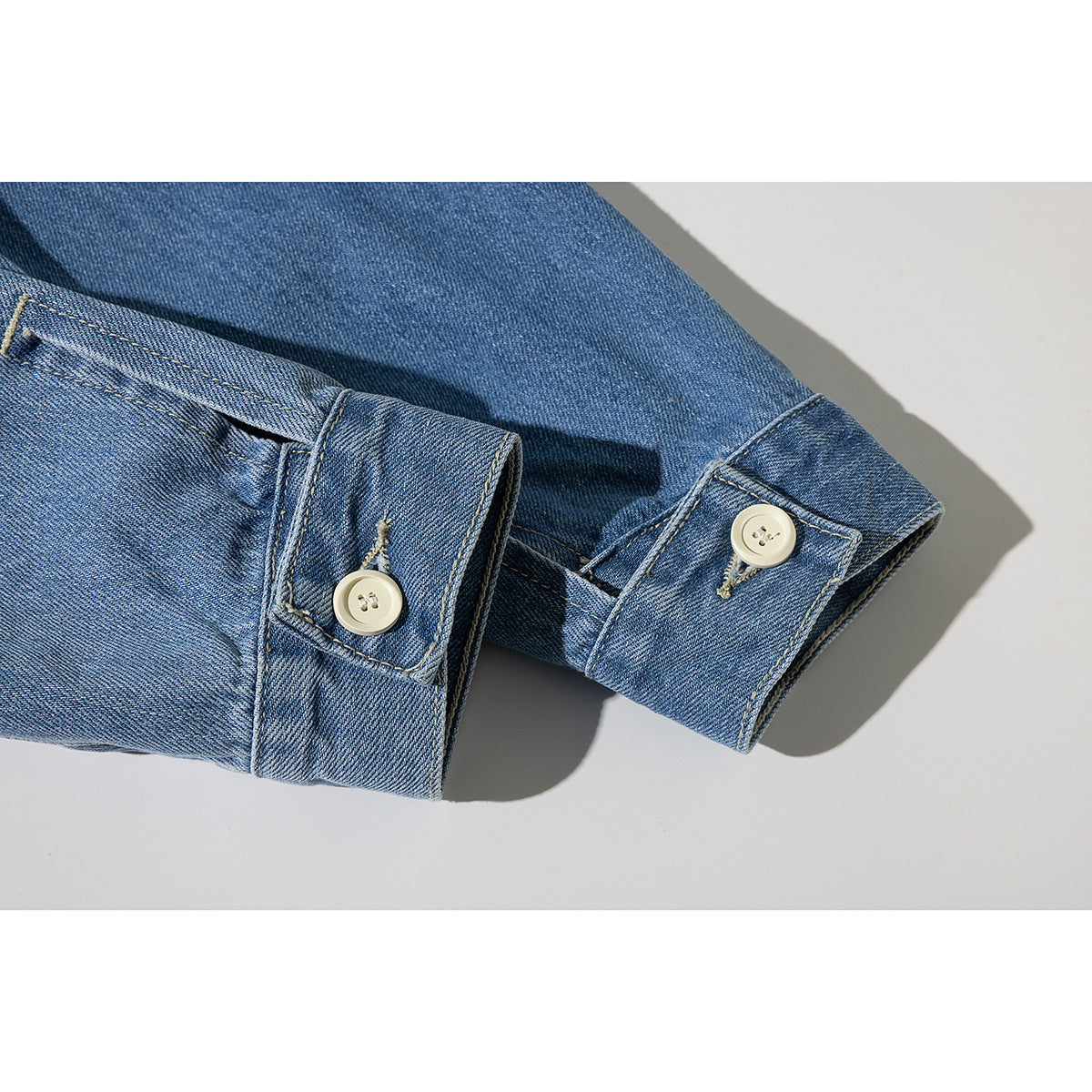 Close-up of a blue denim jacket sleeve cuffs with cream buttons and stitched buttonholes.
