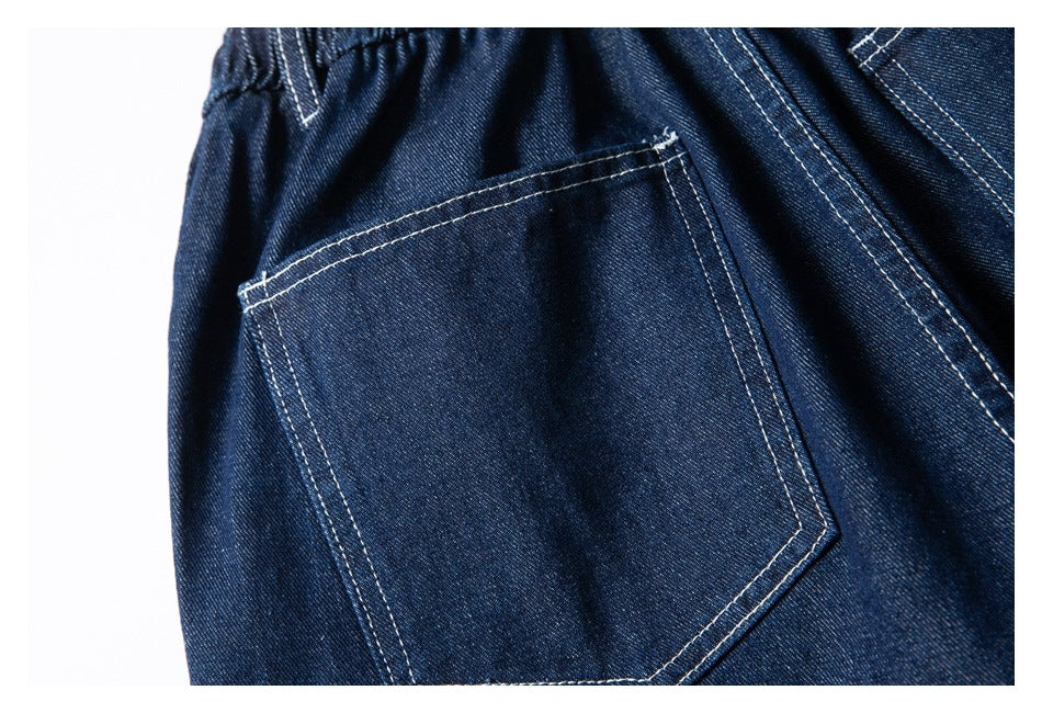 Close-up of a back pocket and waistband detail on dark indigo denim shorts with contrasting white stitching.