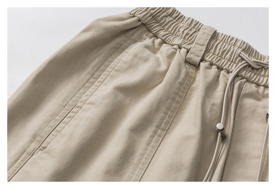 Close-up of beige shorts showing a slanted side pocket, elastic waistband, and drawstring toggle.