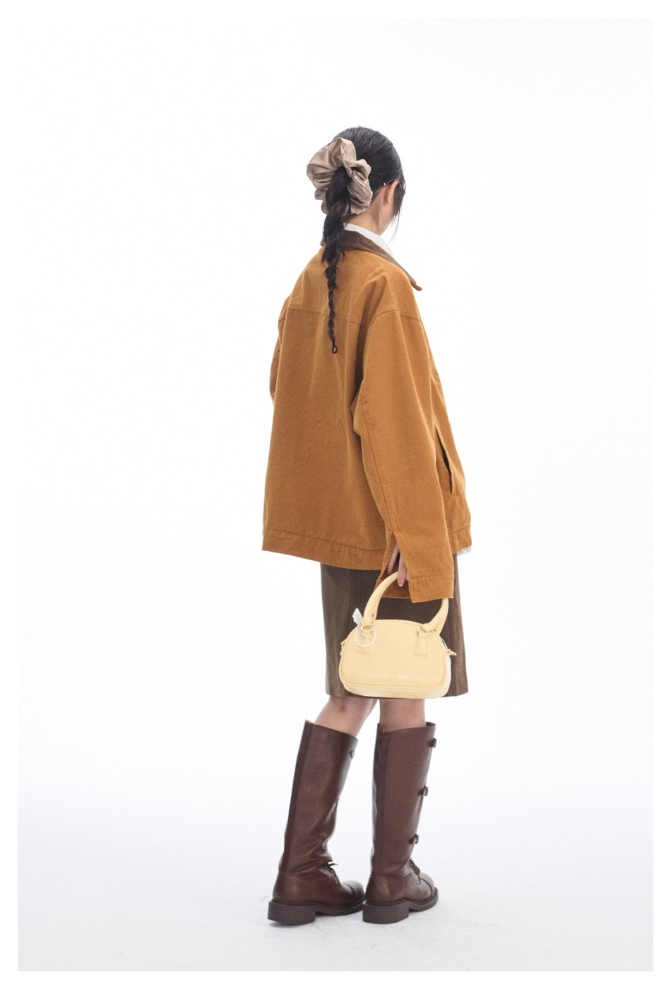Model seen from behind wearing an oversized ochre-brown jacket and brown skirt.