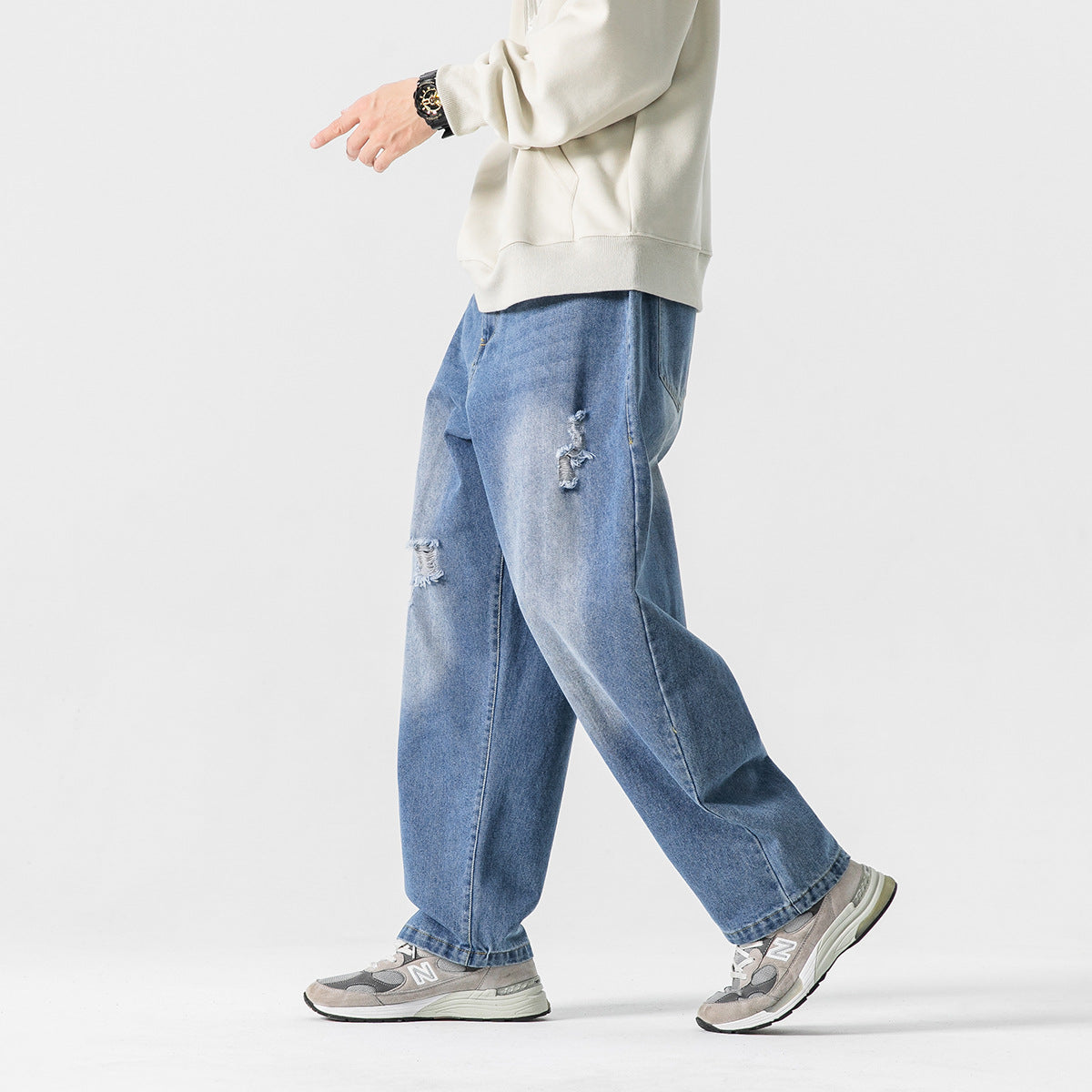 Side view of a model wearing relaxed blue distressed jeans with a cream sweatshirt and gray sneakers.