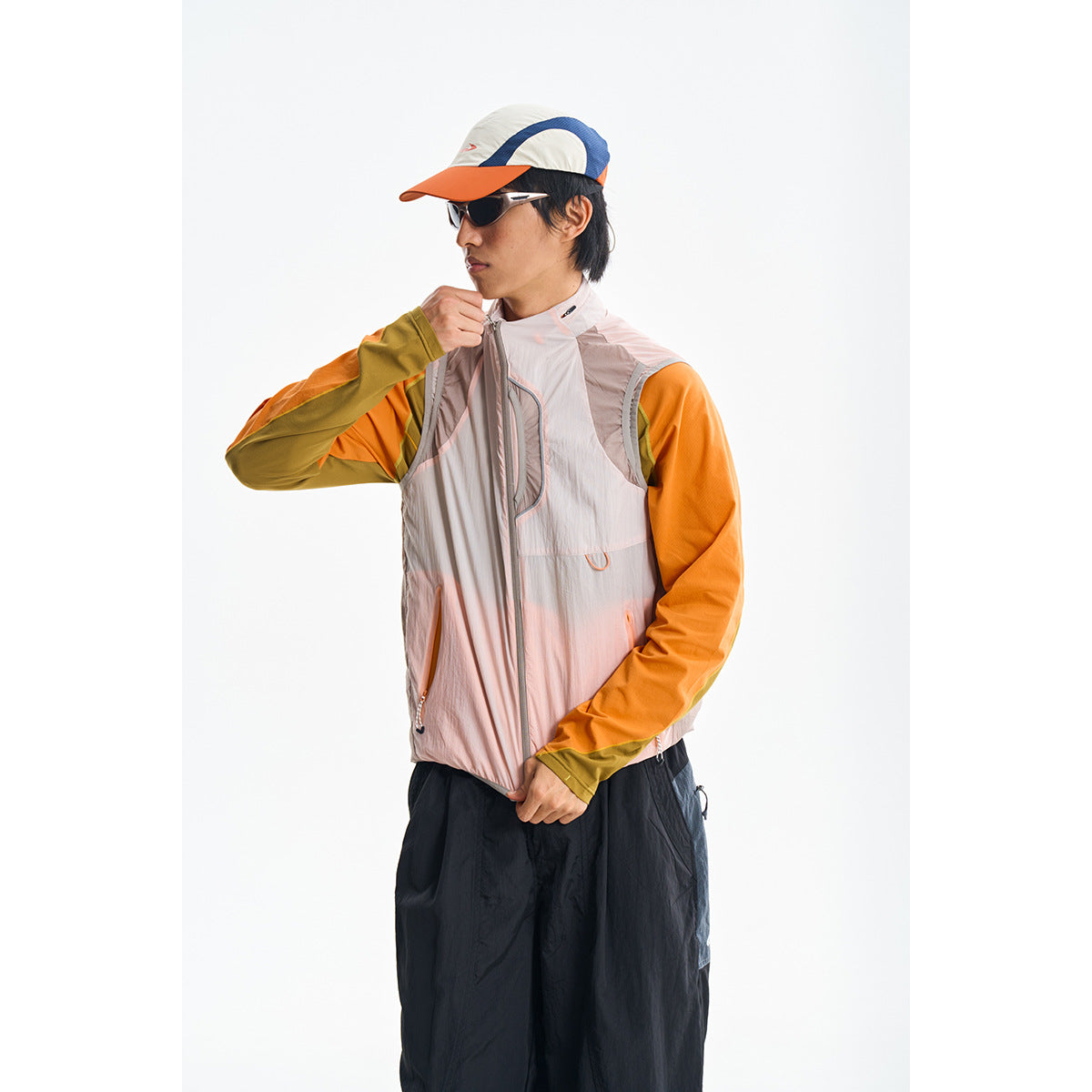 Model wearing a pale pink sleeveless zip vest over an orange and olive long-sleeve top.