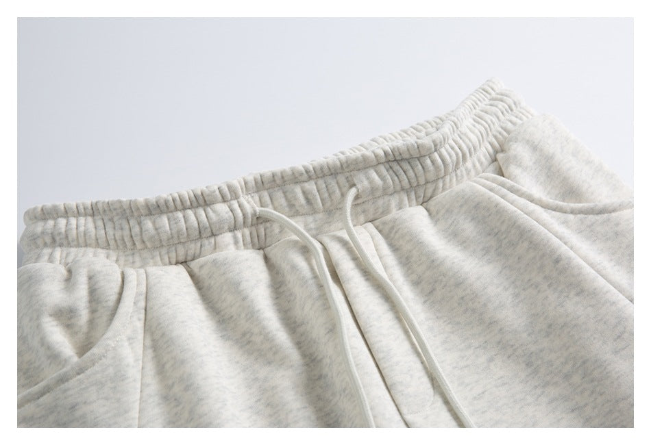 Close-up of light gray heather sweatpants showing the gathered elastic waistband, white drawstring and pocket opening.