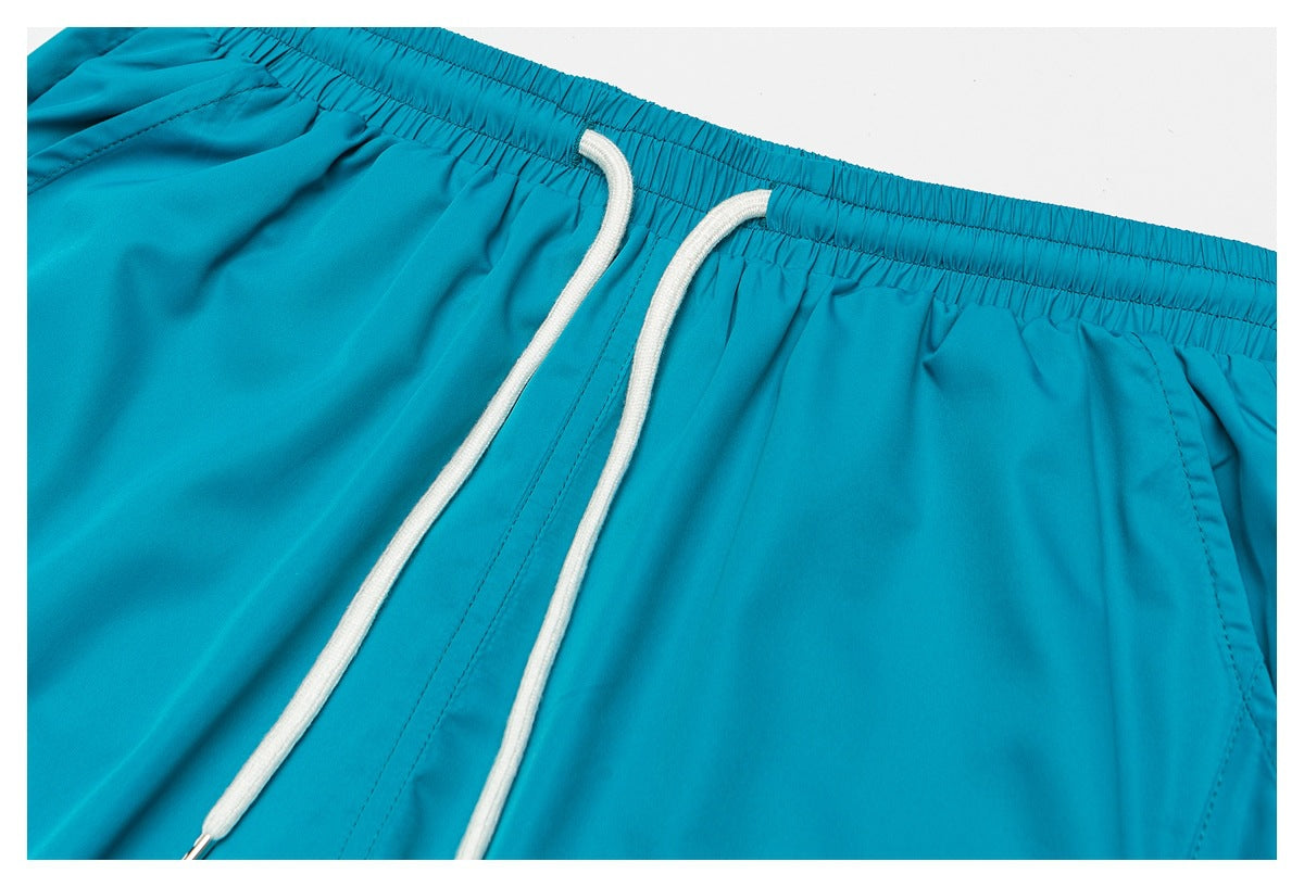 Close-up of turquoise shorts showing the elastic waistband, white drawstrings, and a side pocket opening.