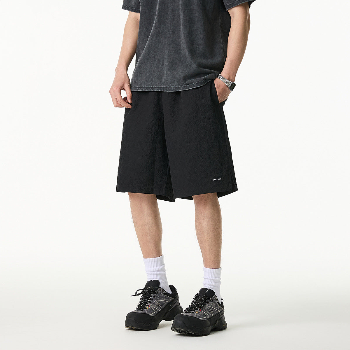 Front view of a model wearing loose black knee-length shorts with a small white hem label.