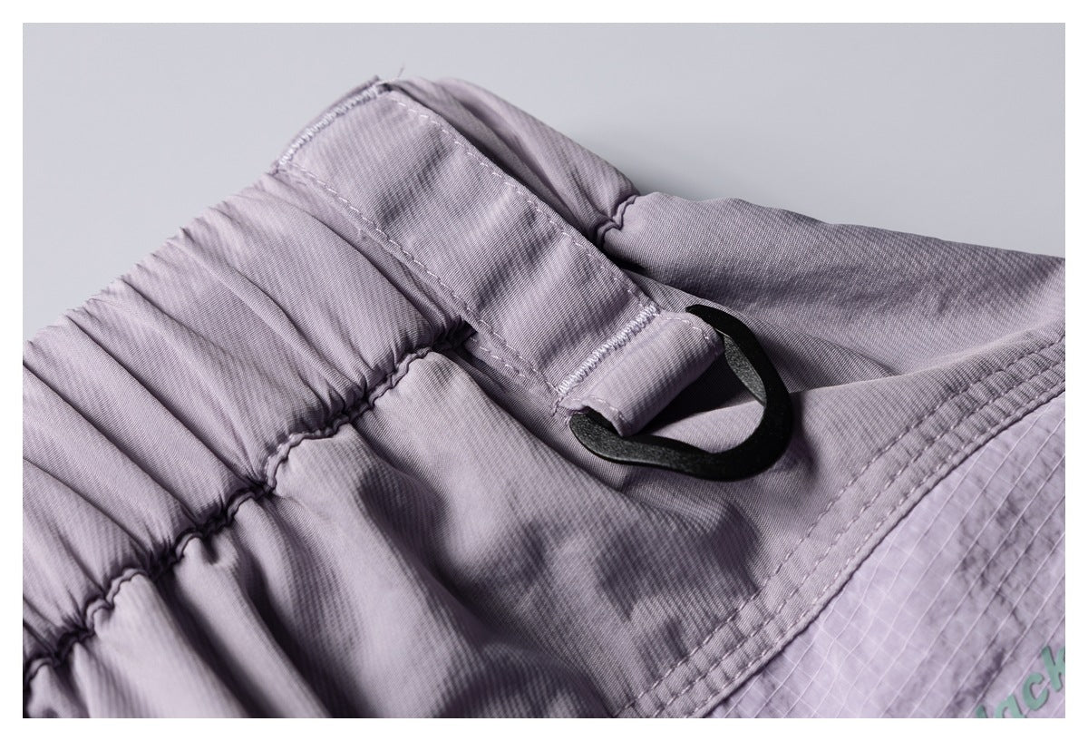 Close-up of a mauve elastic waistband and belt loop with a black hook; partial green lettering appears on the garment.