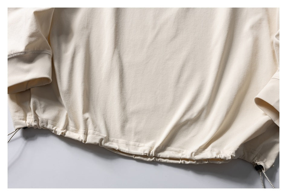 Close-up of the cream sweatshirt’s gathered hem and adjustable side drawcords.