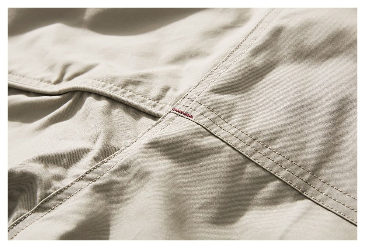 Close-up of a beige jacket showing intersecting stitched seams and a small red bartack.
