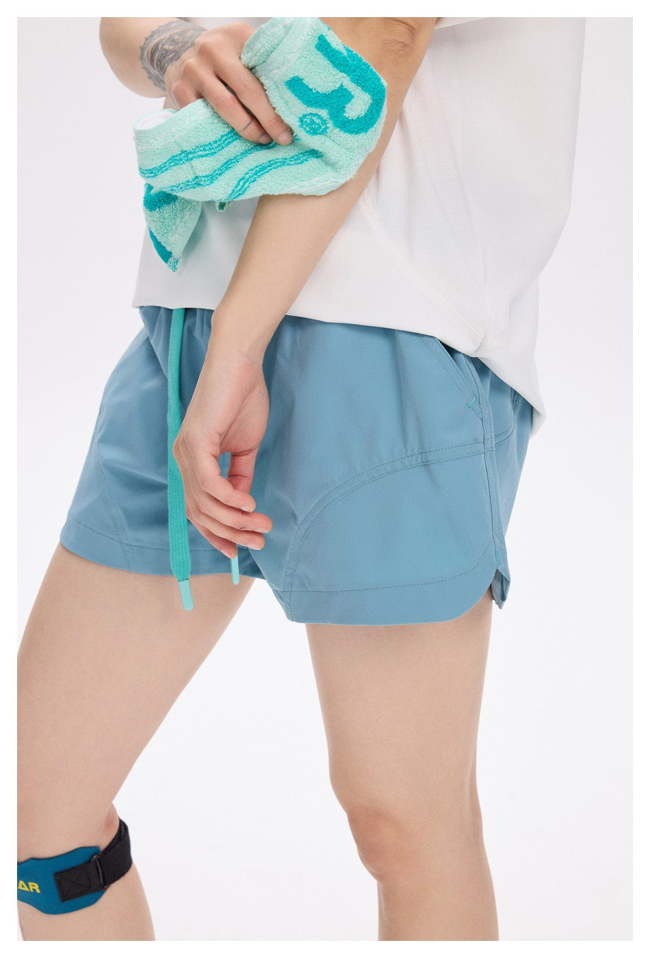 Close-up of light teal running shorts showing the curved side panel, stitching and turquoise drawstring.