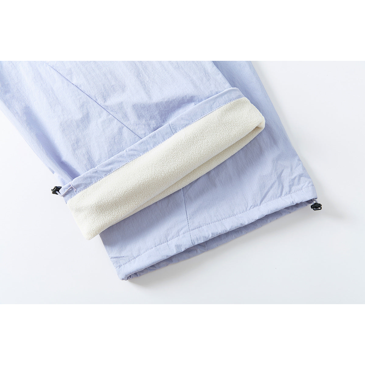 Close-up of a pale lavender pant leg with the hem turned up to show a thick cream-colored lining and adjustment hardware.