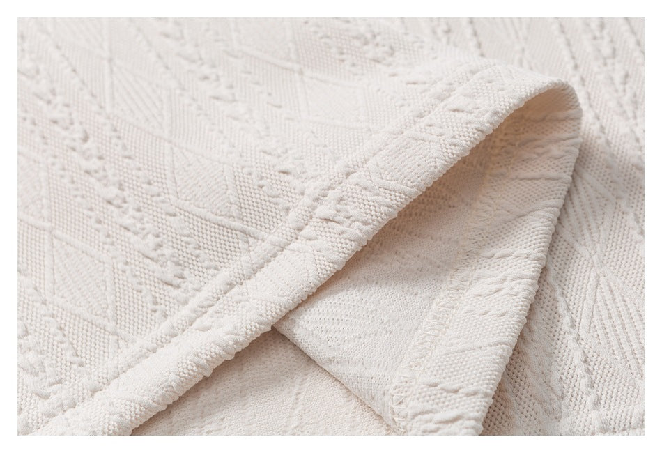Close-up of off-white textured knit fabric with a raised geometric pattern and a folded edge.