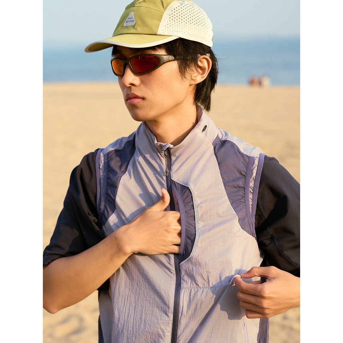 Close view of a model opening the front pocket of a light gray-lavender zip vest with dark contrast panels.