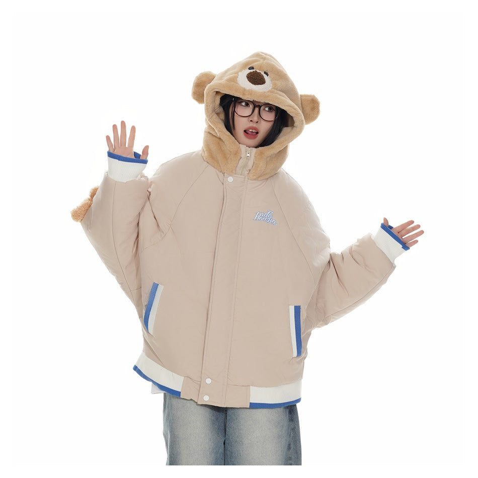 Person wearing a khaki puffer jacket with a bear-face hood, striped trim and jeans, hands raised