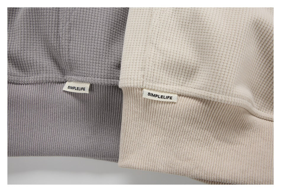 Close-up of gray and cream pullover hems with ribbed bands and sewn SIMPLELIFE labels.