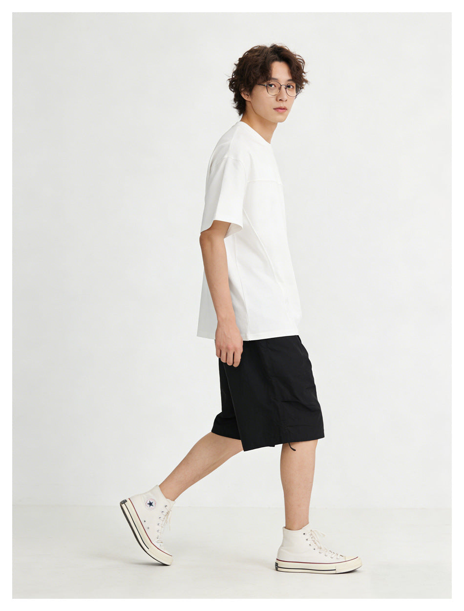 Model in profile wearing a white oversized short-sleeve T-shirt with a horizontal chest seam.