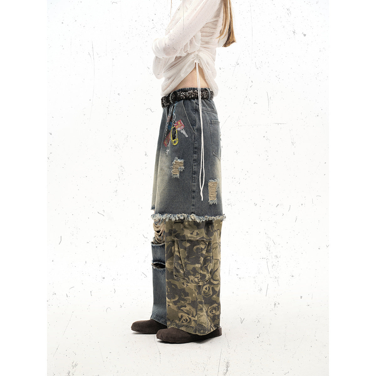 Side view of a model wearing oversized distressed gray denim pants with a frayed hem and olive camouflage cargo panels.