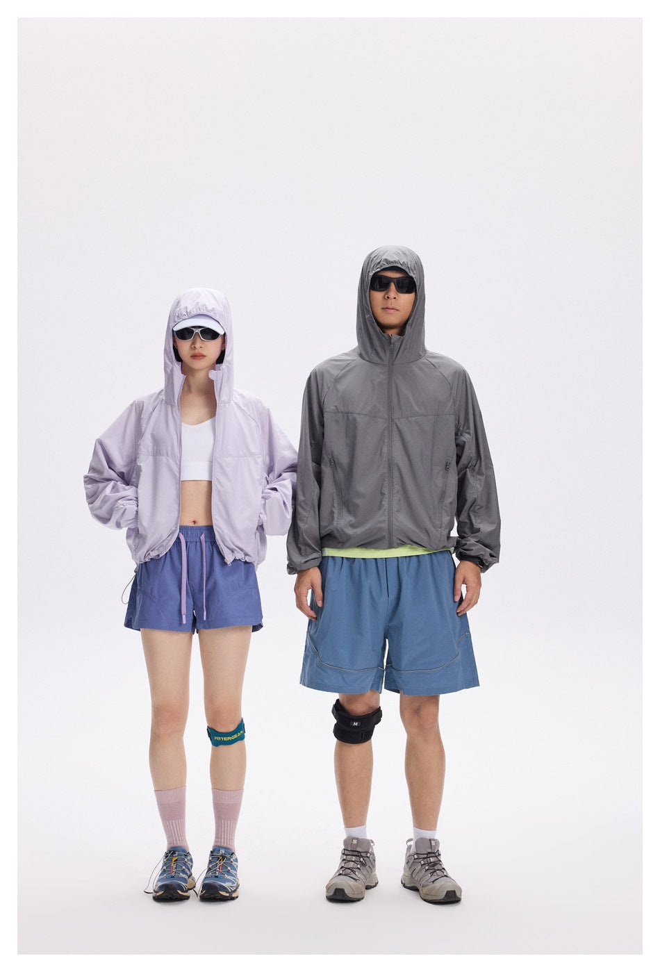 Two models wear hooded jackets: one pale lavender and one charcoal gray, paired with blue shorts.