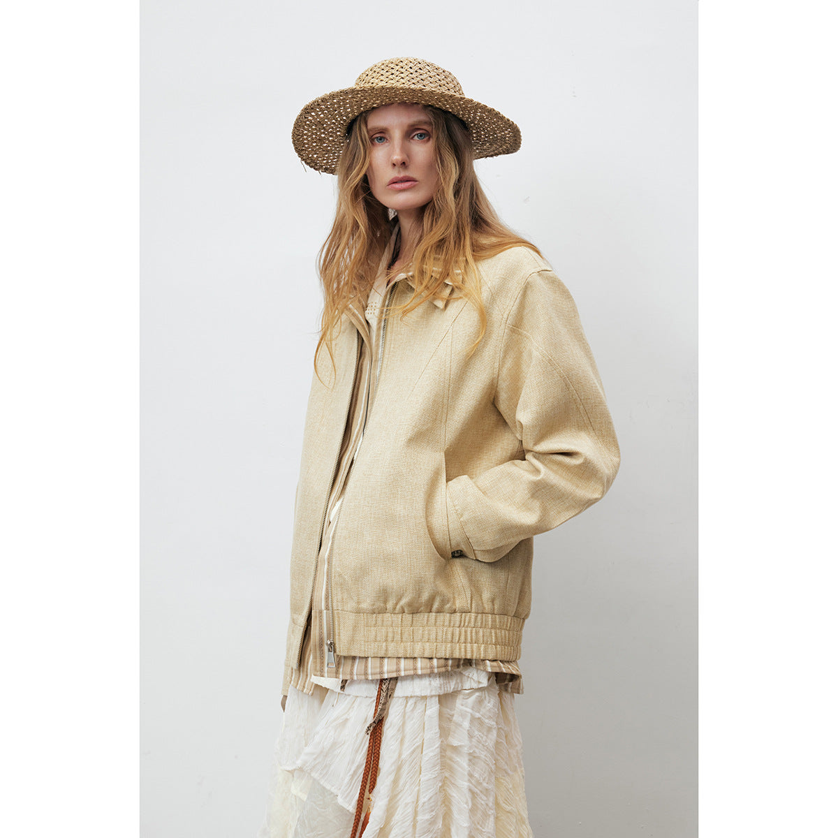 Model in a pale beige zip-front jacket with elasticated hem, layered over white clothing.
