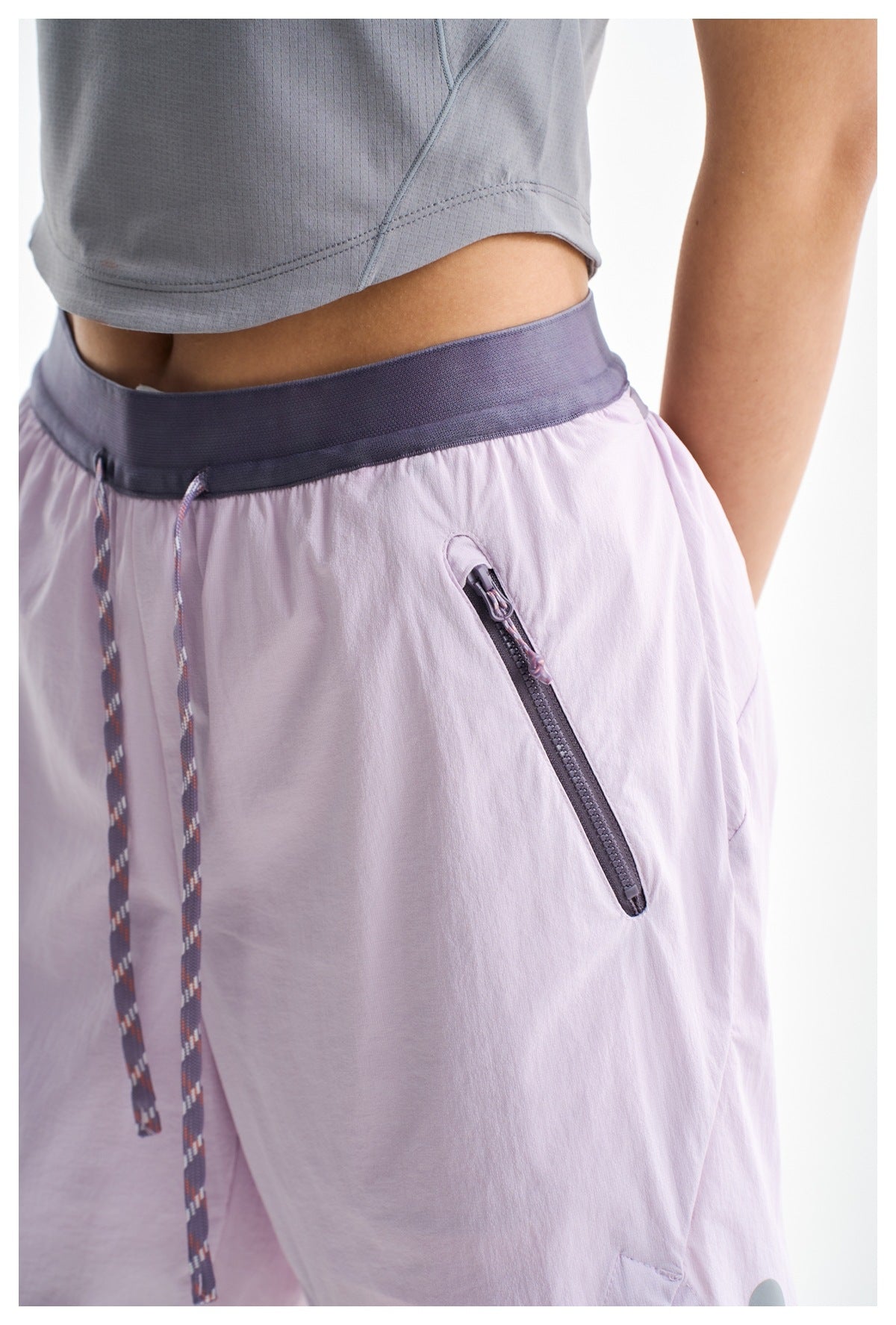 Close-up of lilac shorts showing the dark waistband, patterned drawcord and angled zip pocket.