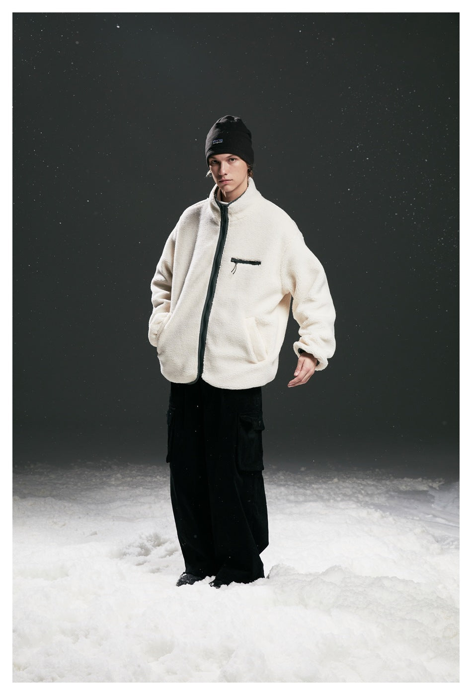 Full-length model wearing a cream fleece zip jacket with dark trim and chest pocket, black beanie, and loose black cargo