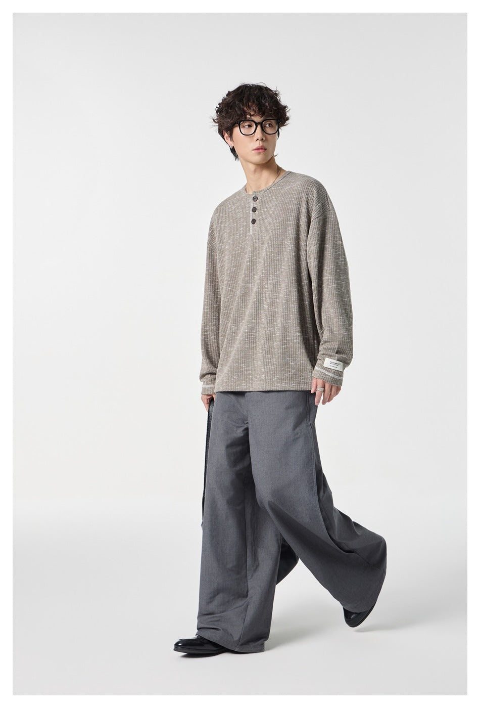 Model wearing a light taupe-gray Henley with a three-button placket and gray wide-leg trousers.