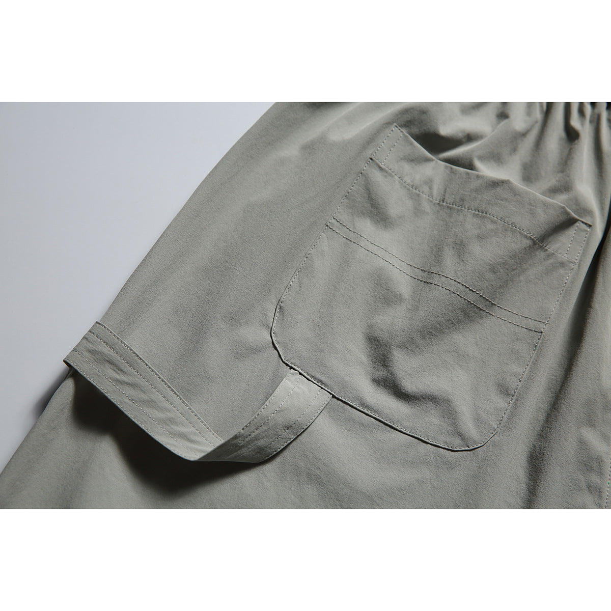 Close-up of a large stitched patch pocket on the back of gray-green shorts.