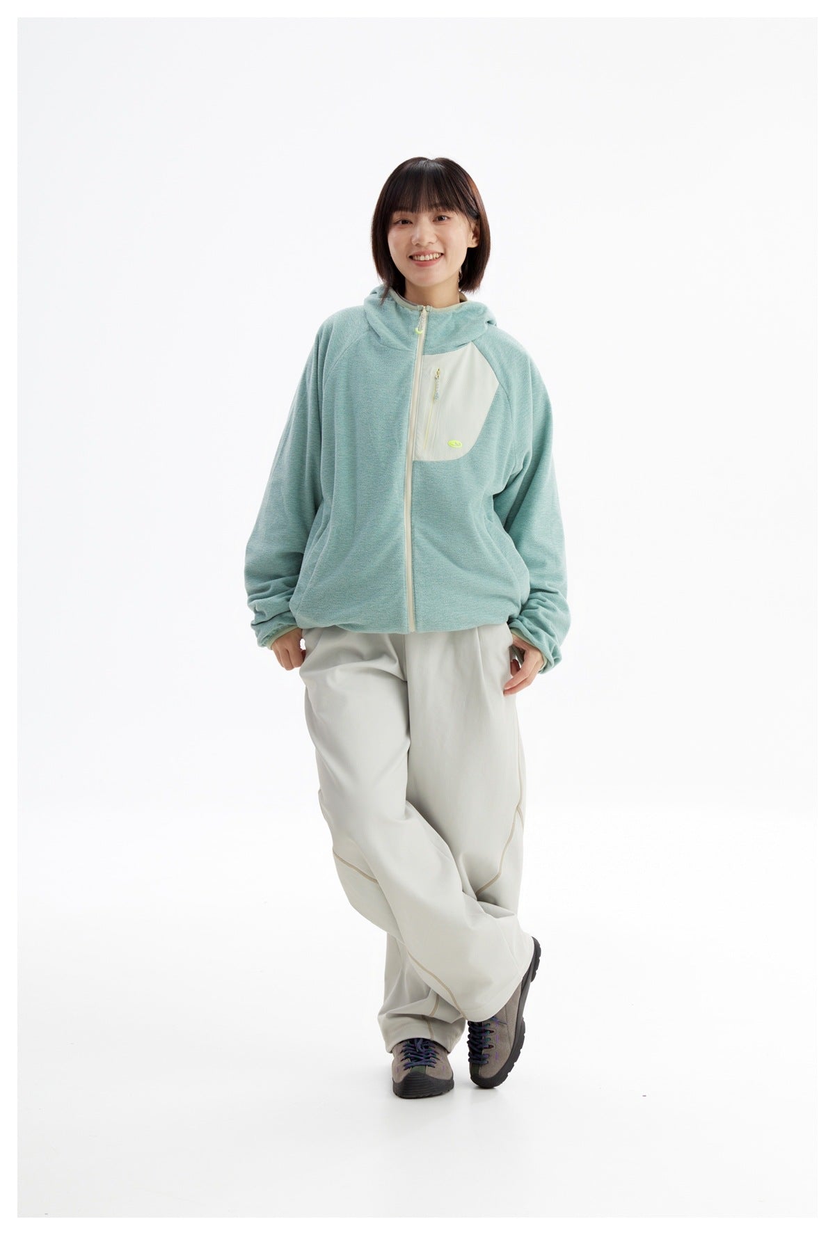 Model posing in a mint-green hooded zip jacket with a cream chest panel and loose ivory pants.