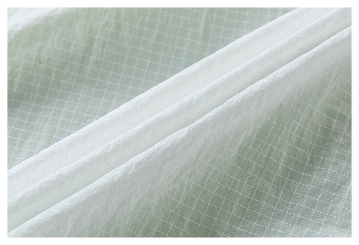 Close-up of pale gray-white fabric with a fine grid pattern draped in soft folds.