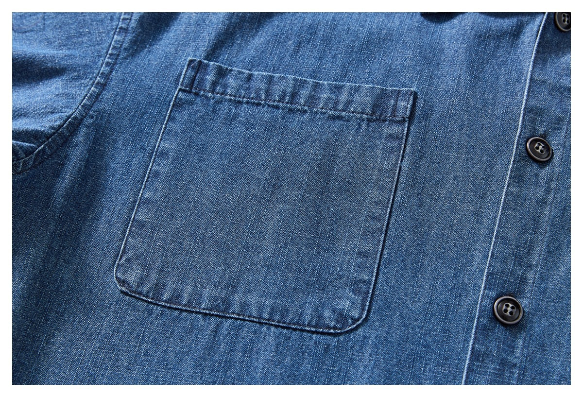Close-up of a blue denim shirt’s plain chest pocket and dark buttons.