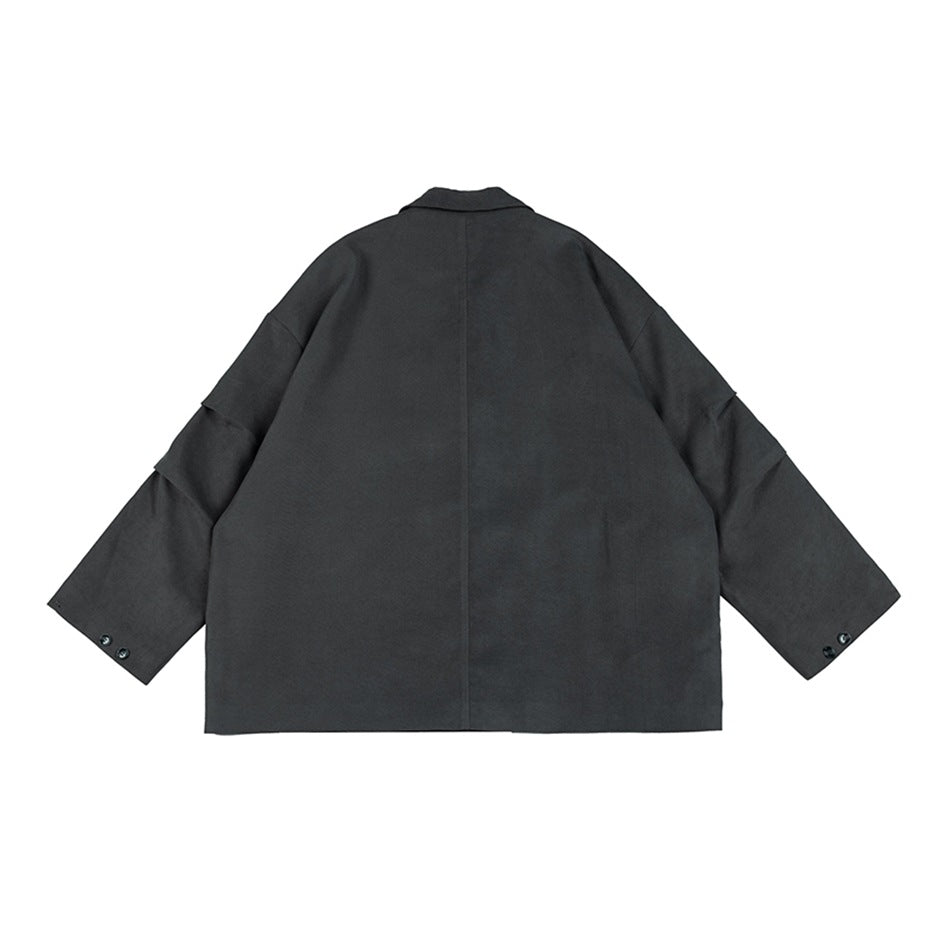 Back view of a charcoal-gray oversized blazer with a center seam, broad sleeves, and buttoned cuffs on white.