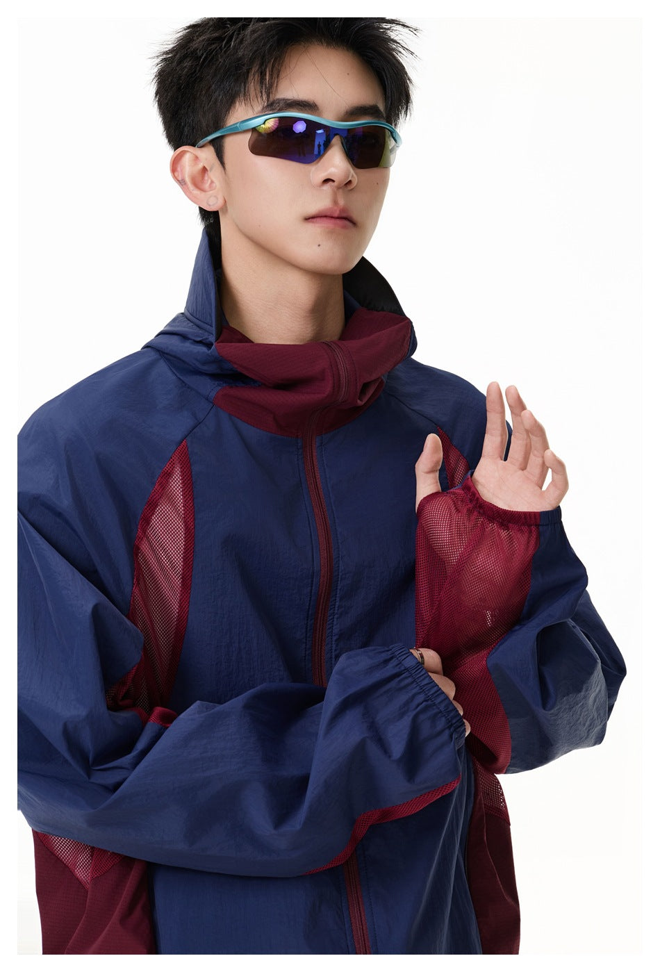 Model wearing a navy and burgundy color-block hooded jacket with mesh panels and mirrored sunglasses.