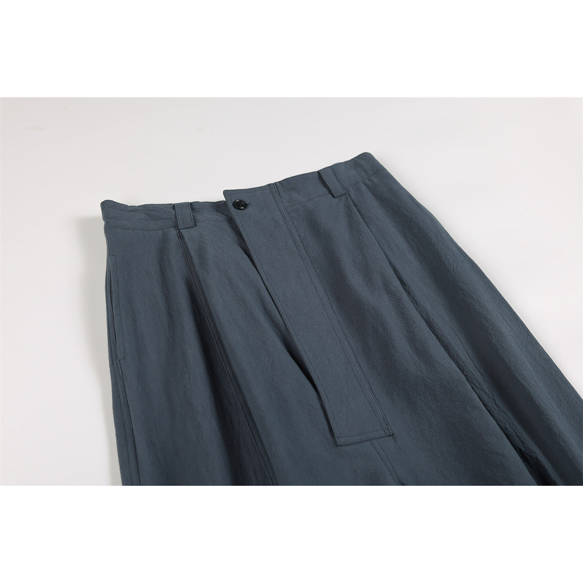 Close-up of dark slate-blue trousers showing the waistband, buttoned fly, belt loops and side pocket.
