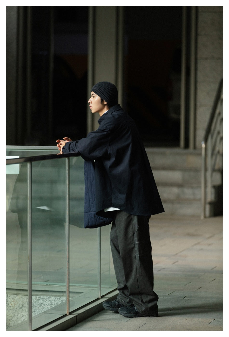 Side and back view of a model in an oversized black shirt, gray wide-leg trousers, and a black beanie.