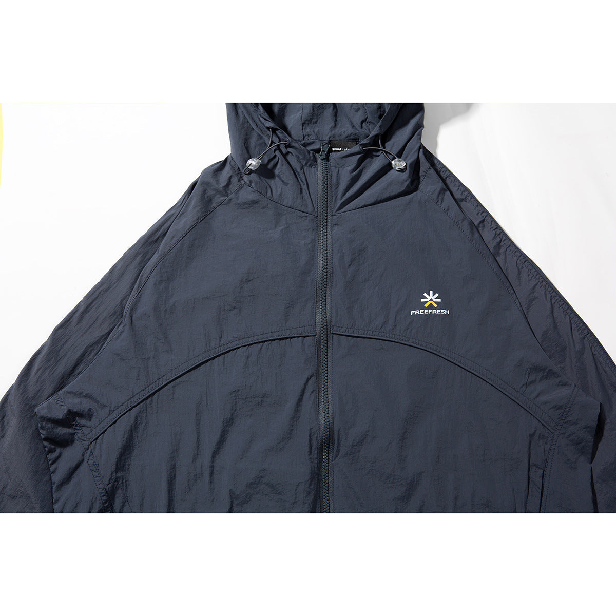 Close-up of a dark navy hooded jacket front, showing the zipper, hood drawcords, curved seams and small chest logo.