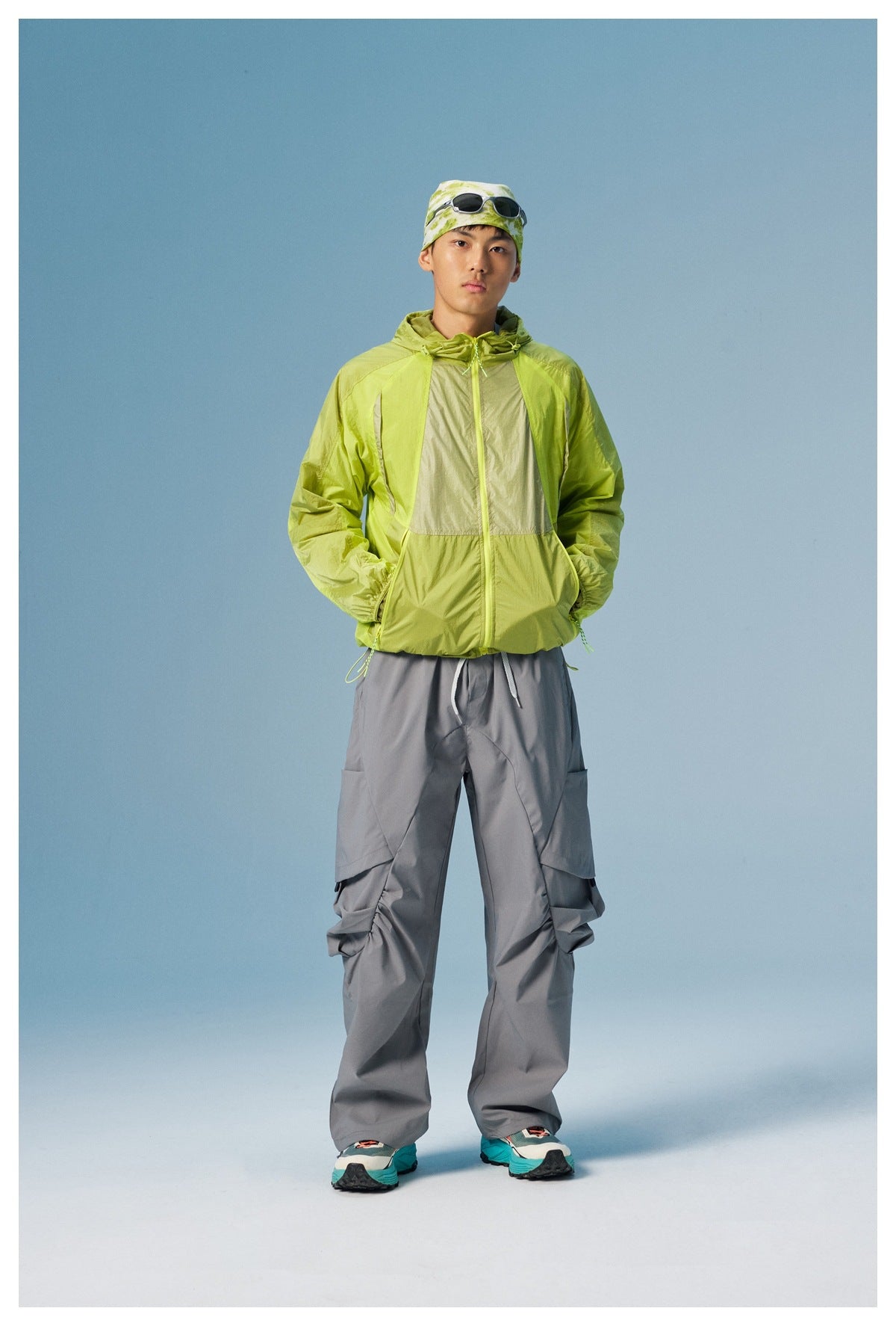 Front view of a man wearing a lime green color-block hooded jacket and loose gray cargo pants.