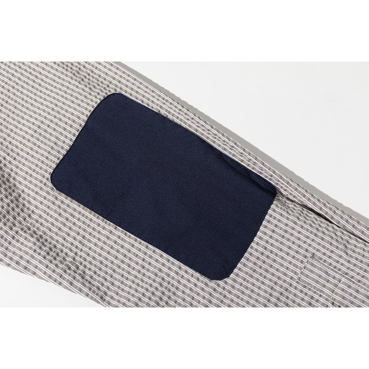 Close-up of a dark navy rectangular patch on the taupe-and-white striped shirt.