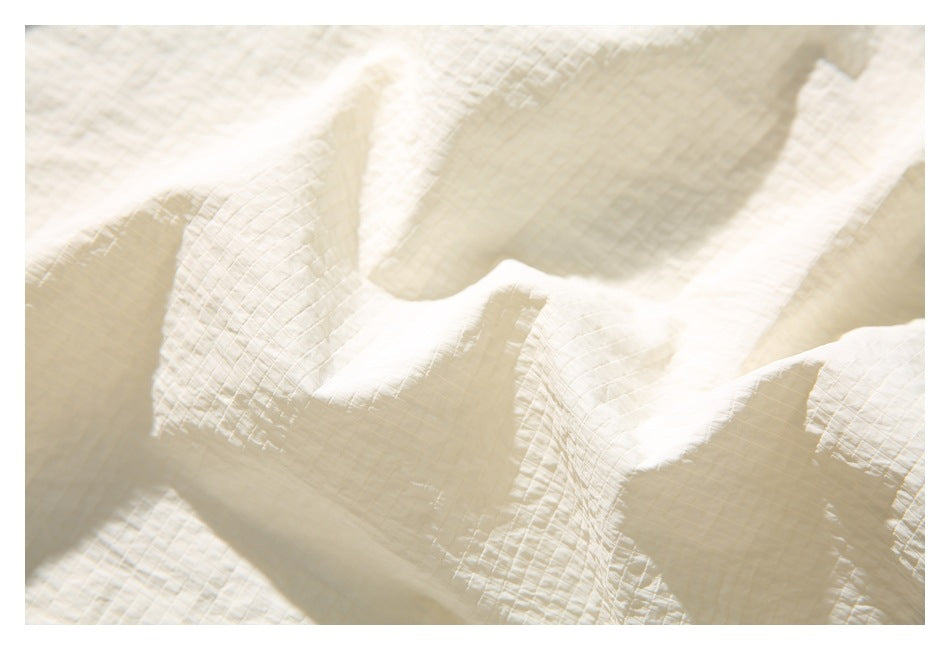 Close-up of softly folded cream fabric with a fine crinkled grid texture.