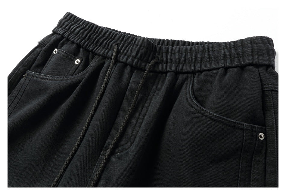 Close-up of black pants showing the elastic drawstring waist and front pockets with silver rivets.